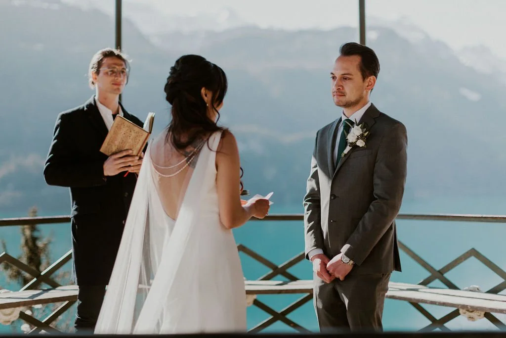 A couple getting married on a balcony overlooking mountains, with a woman officiant holding a book.