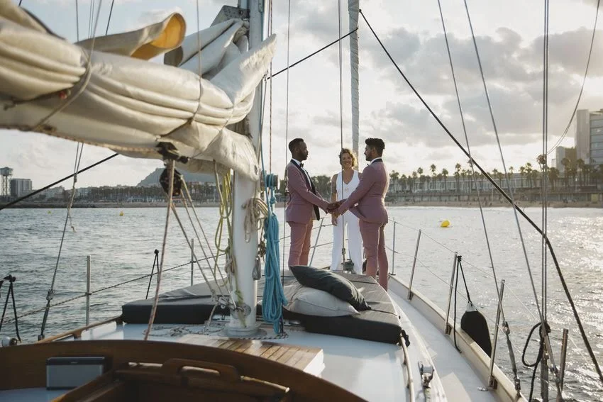 A couple getting married on a sailboat with a officiant during sunset, with the city skyline and palm trees in the background.