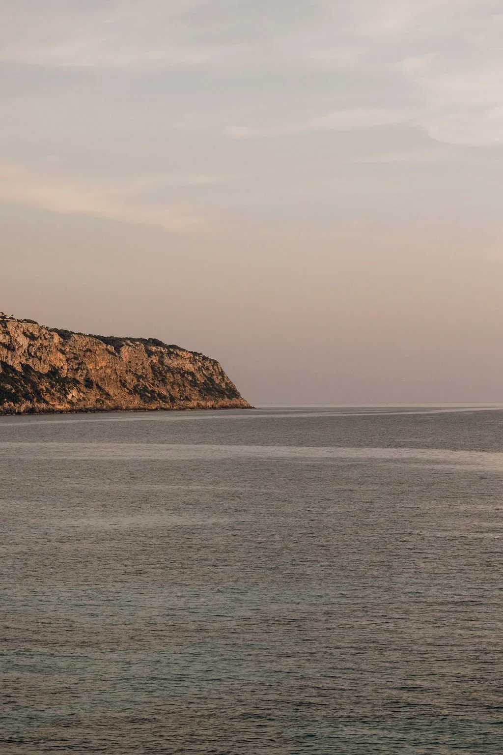 Calm ocean waters with a rocky coastline on the left side under a partly cloudy sky.