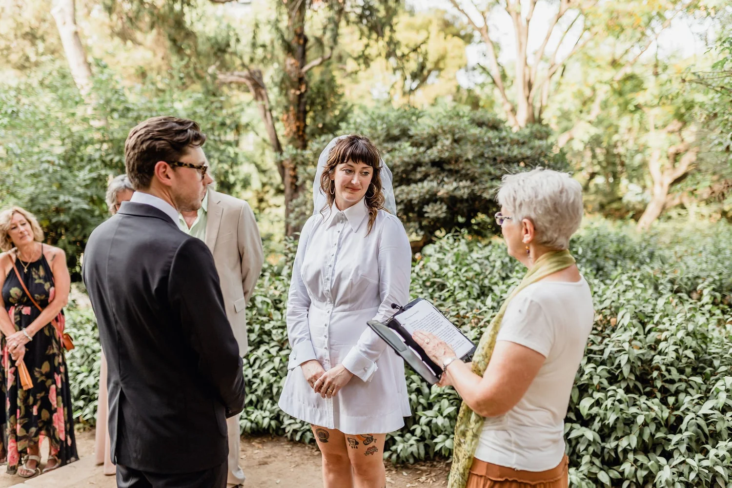 A wedding ceremony outdoors with a bride and groom exchanging vows, surrounded by guests in a lush garden setting.