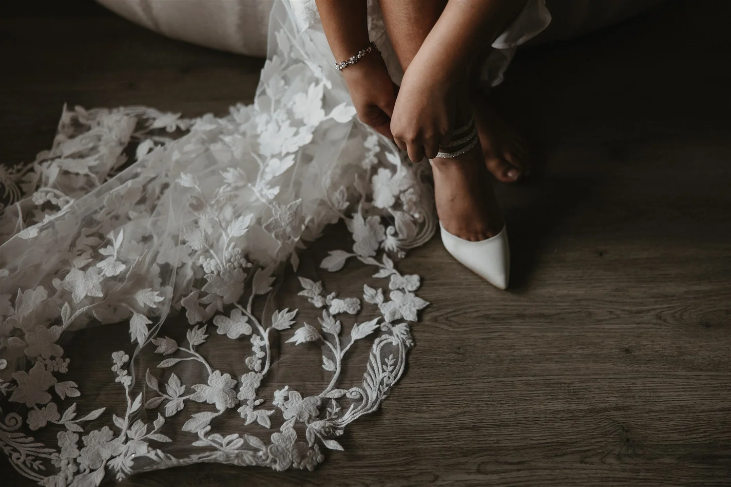 A woman in a wedding dress is adjusting her shoe as lace from her dress decorates the floor.