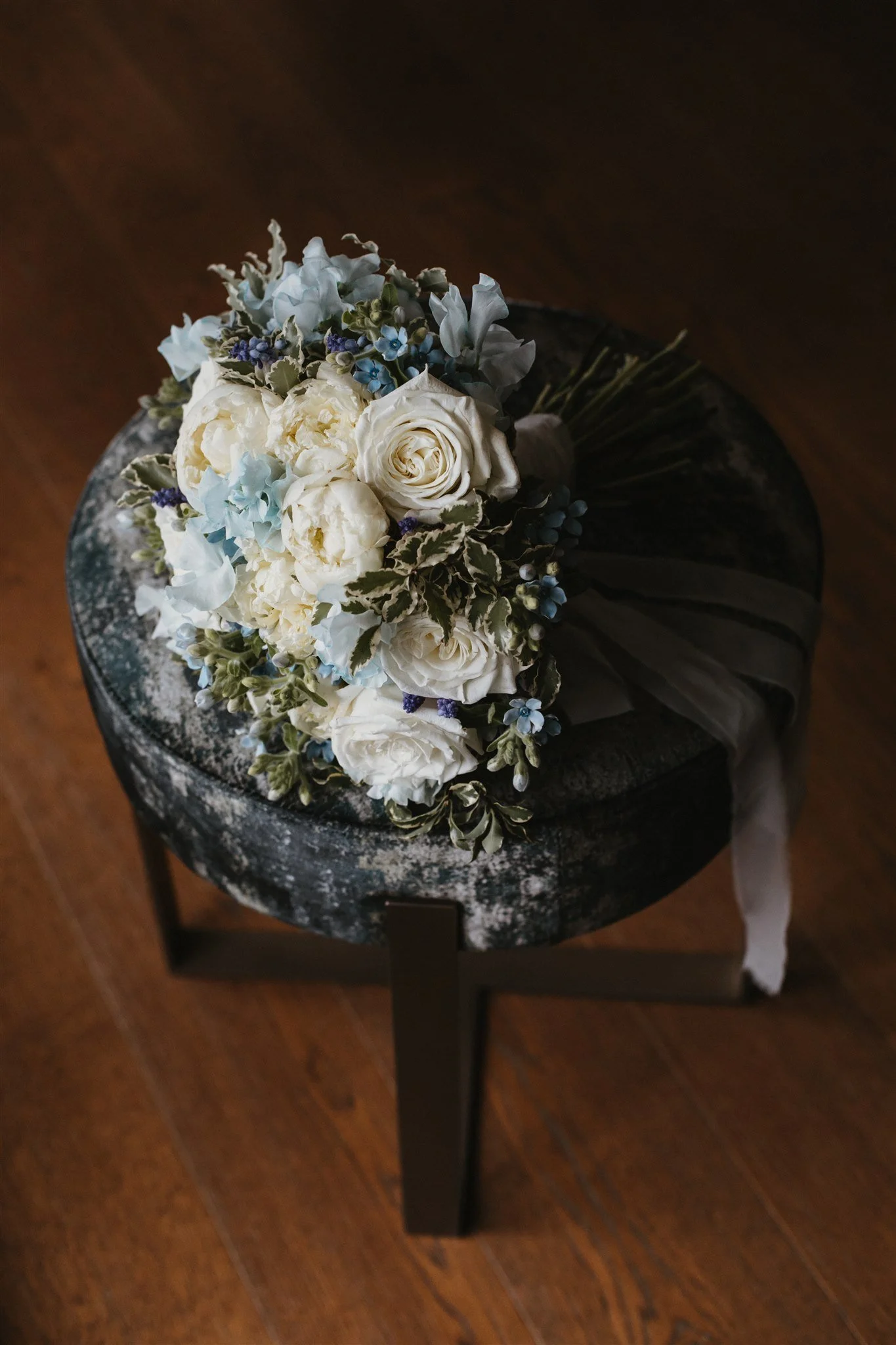 A bouquet of white and light blue flowers on a black and gray marbled round table with a dark wooden floor background.