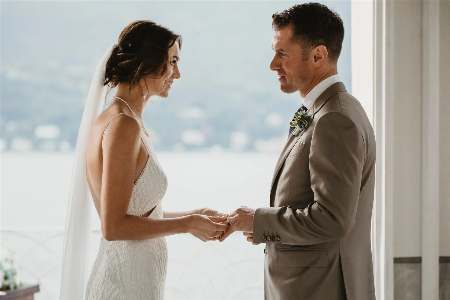 A bride and groom holding hands and gazing into each other's eyes during their wedding ceremony indoors.