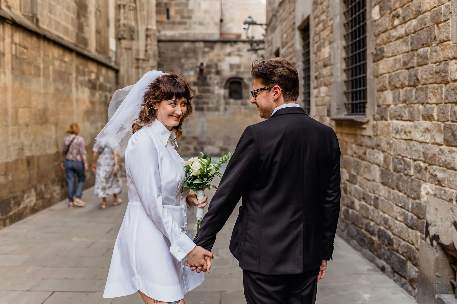 A bride and groom holding hands and smiling at each other in a narrow stone alleyway