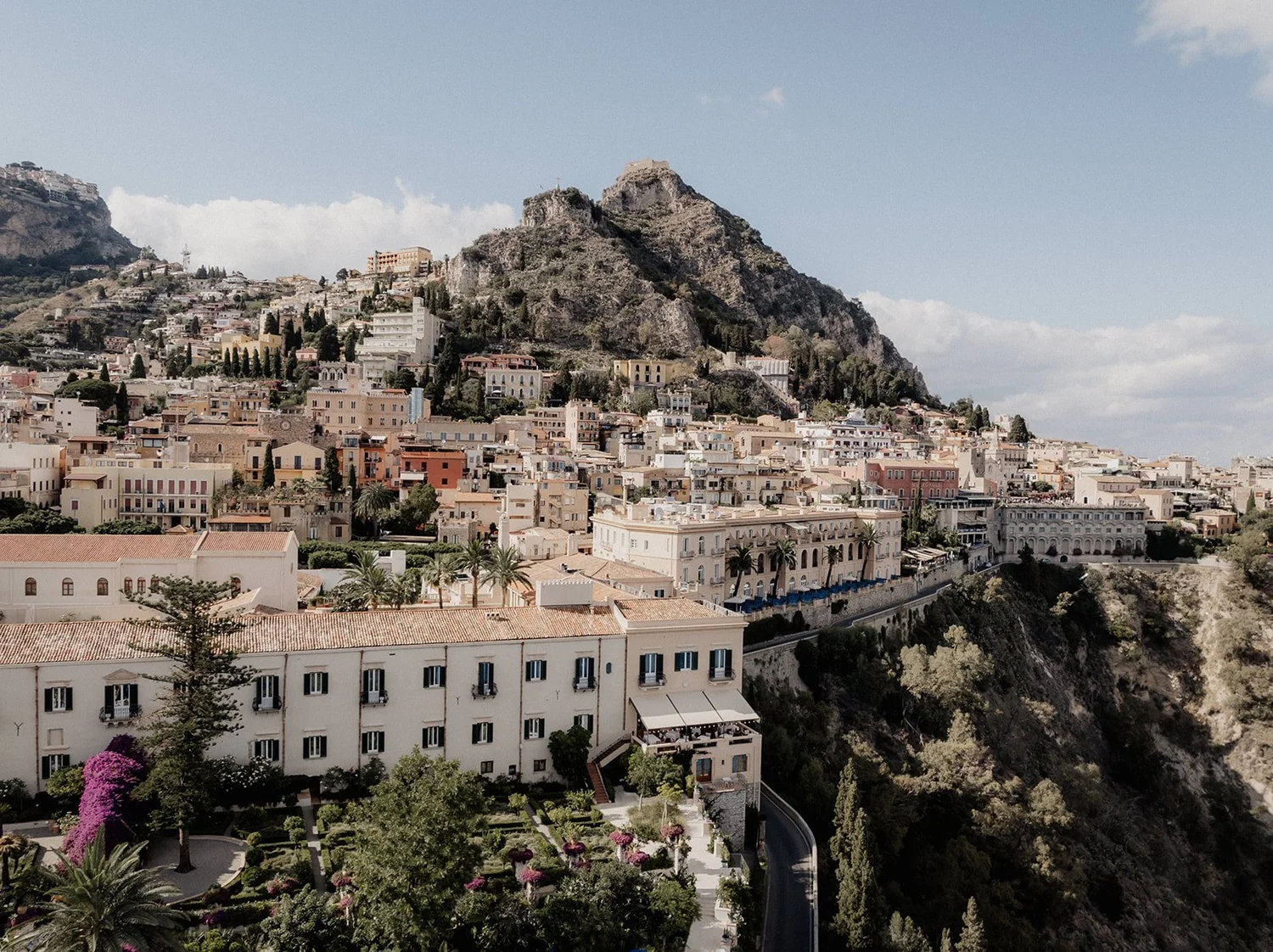 A hillside cityscape with densely packed buildings, a rocky mountain, and a clear sky.