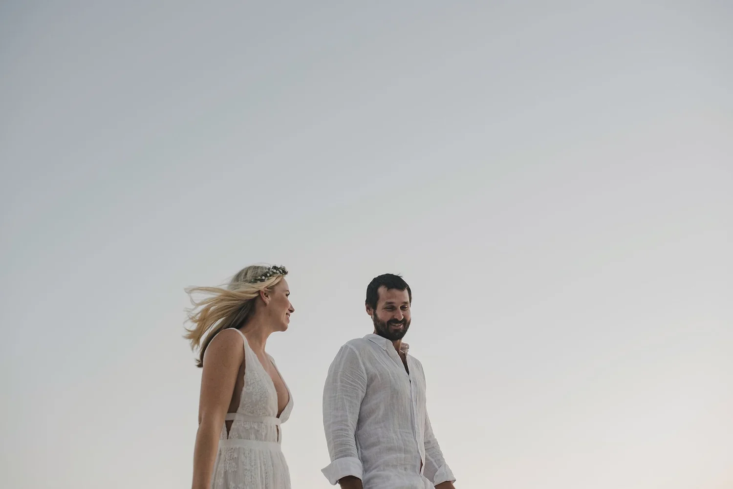 A man and woman walking outdoors on a cloudy day, both smiling and holding hands.