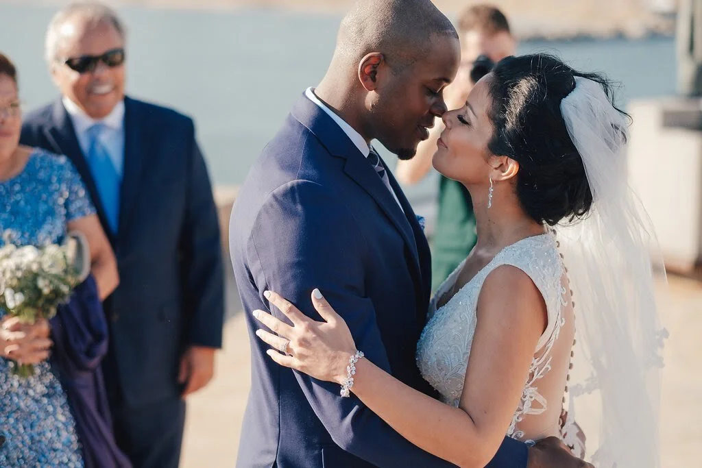 A bride and groom sharing a close, intimate moment during their wedding, with family members in the background.