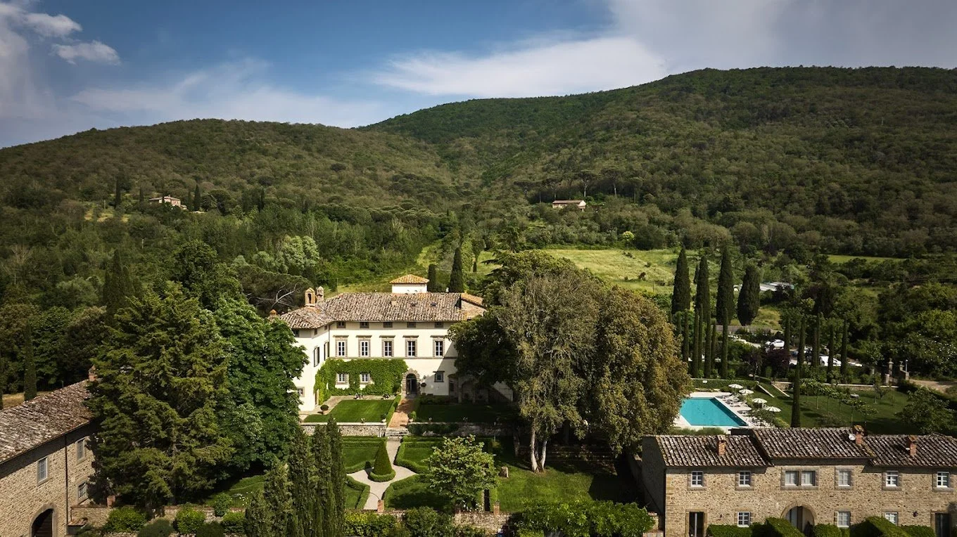 A large estate or villa with a swimming pool, surrounded by trees and hills in the background.