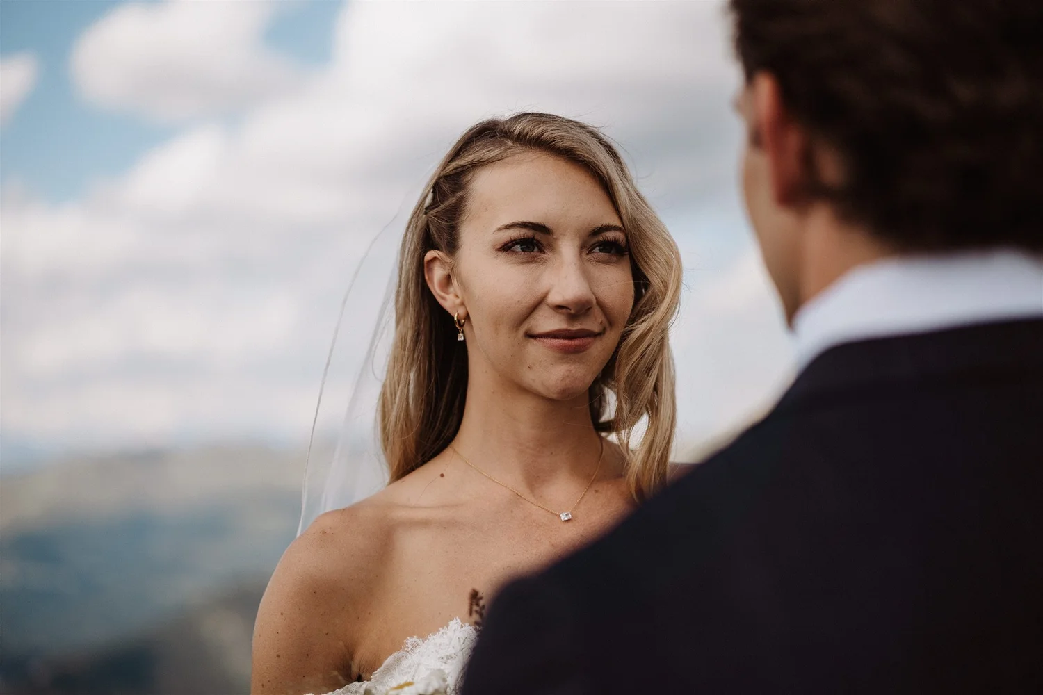 A woman in a wedding dress looks at a man in a suit during an outdoor wedding ceremony.