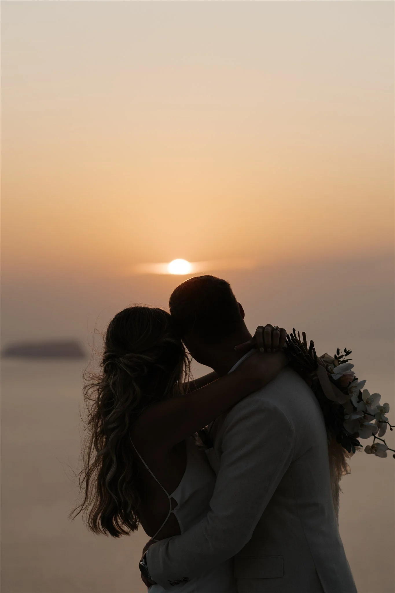 A couple embracing during a sunset, with their faces close and arms wrapped around each other.