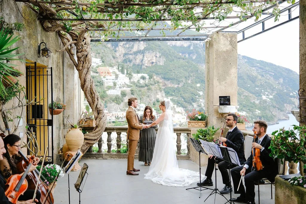 A wedding ceremony on a terrace overlooking a river and mountains, with a string ensemble playing music.