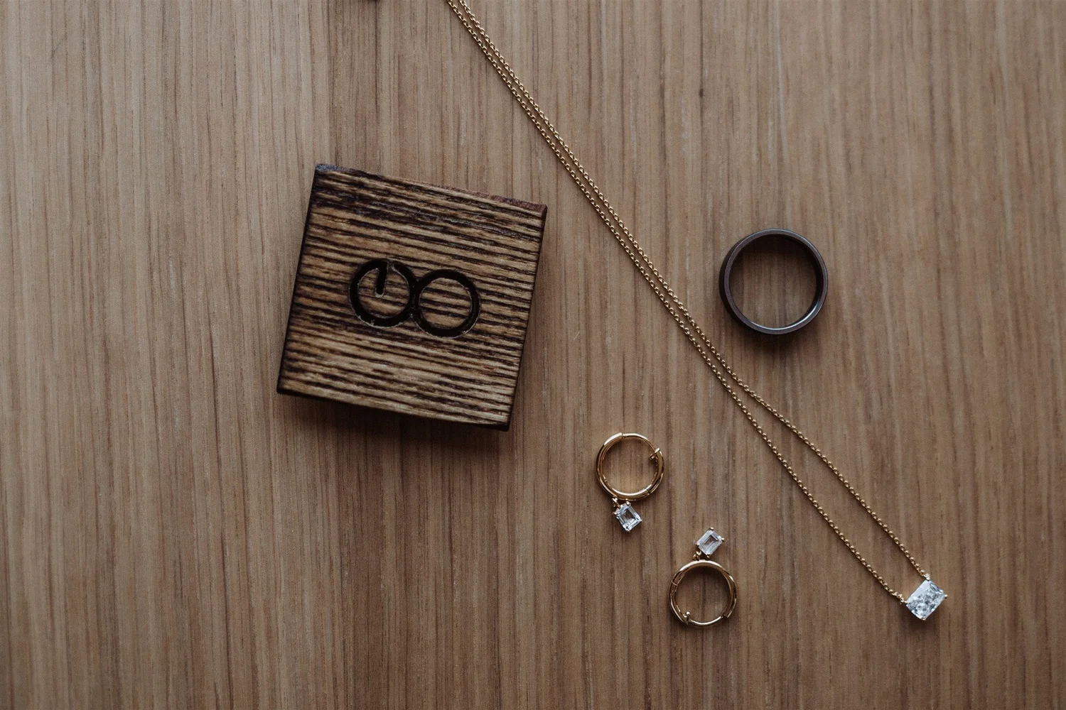 Various jewelry items including a gold chain, rings, and earrings, placed on a wooden surface, along with a small wooden block.