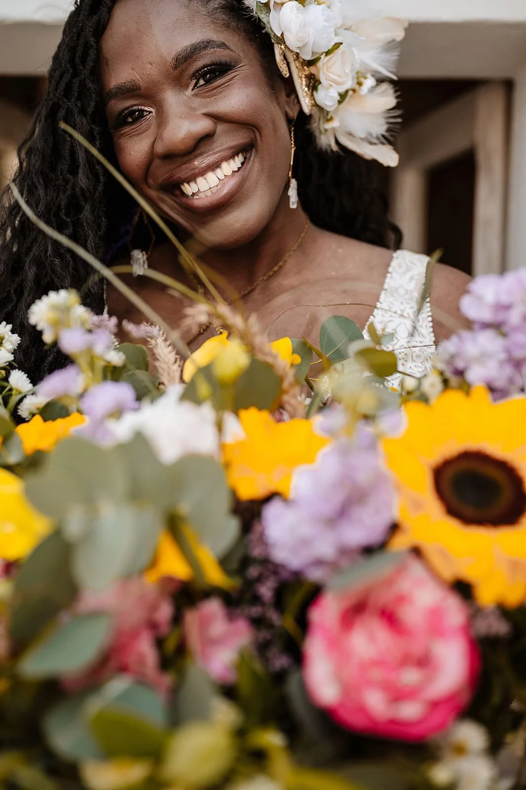 A woman smiling, surrounded by a colorful bouquet of flowers, with white flowers in her hair.