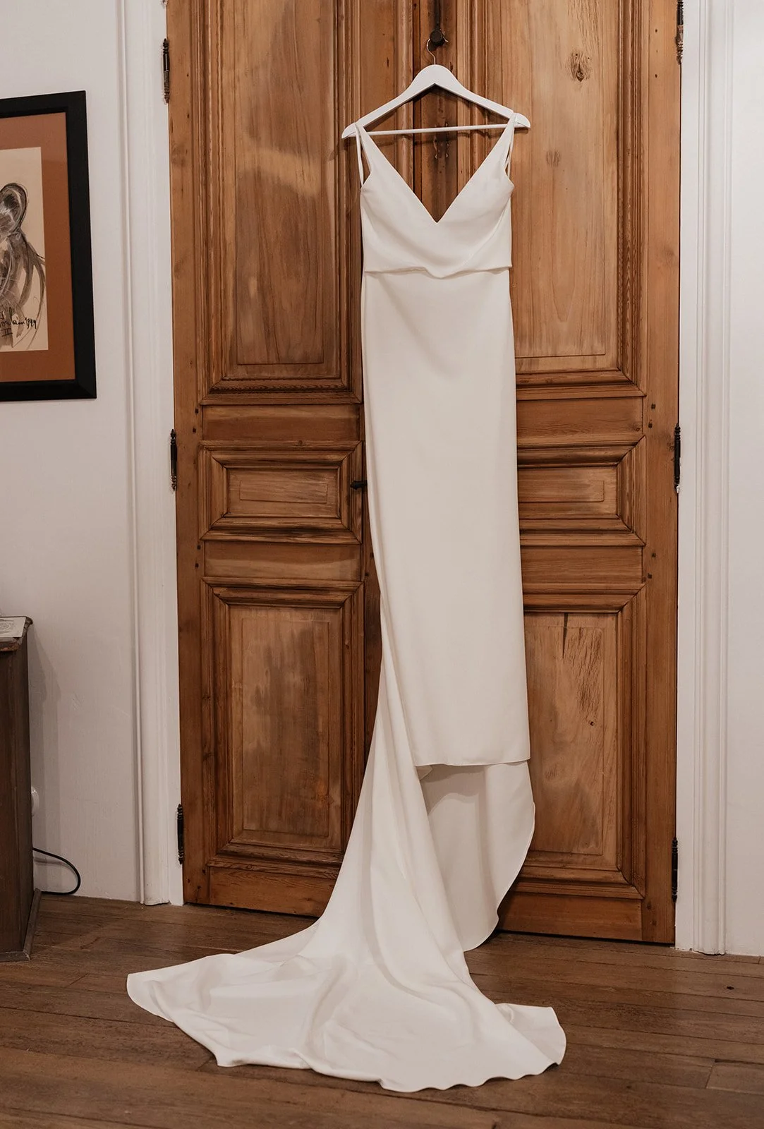 Elegant white wedding dress hanging on a wooden door, with a train pooling onto the floor.