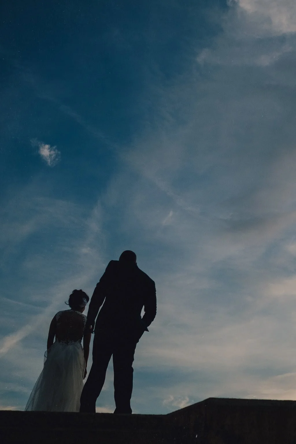 Silhouette of a couple walking together against a sunset sky, with clouds and airplane contrails visible.