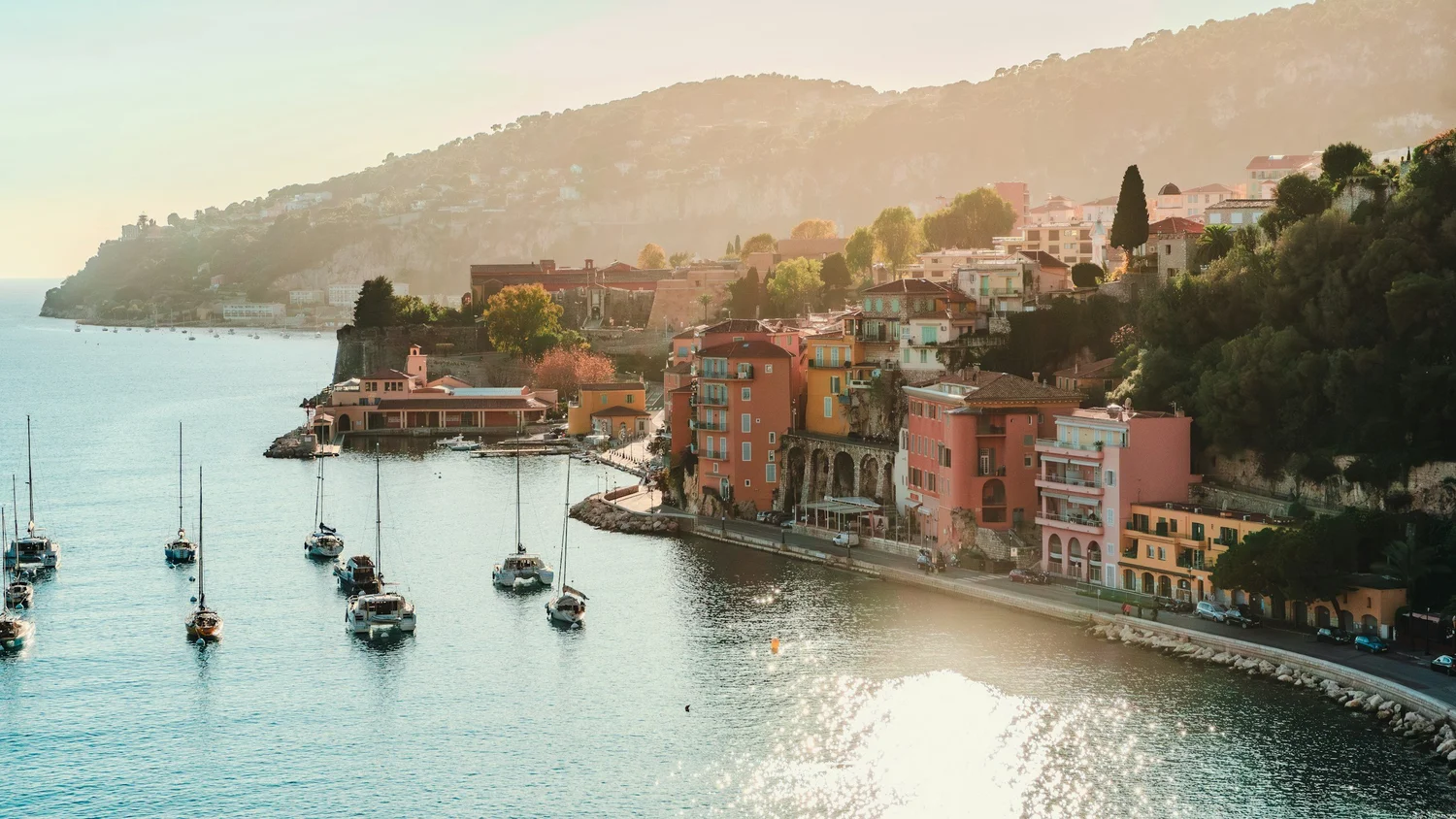 A scenic view of a coastal town with colorful buildings along a hillside and boats docked in the water, with a mountain in the background.