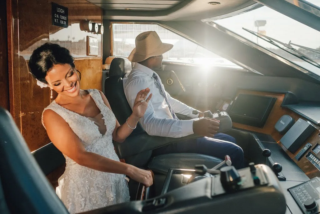 A bride laughing and holding the arm of a pilot inside an airplane cockpit during daytime.