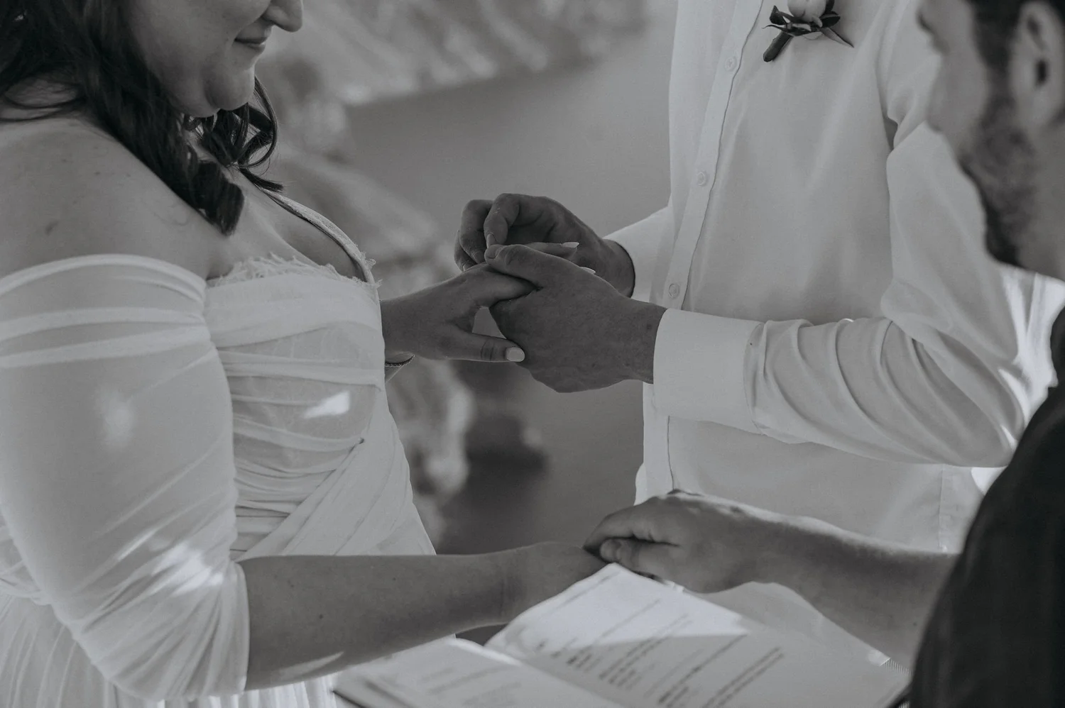 A woman is getting married, her hand is held by the officiant who appears to be placing a ring on her finger in a wedding ceremony.