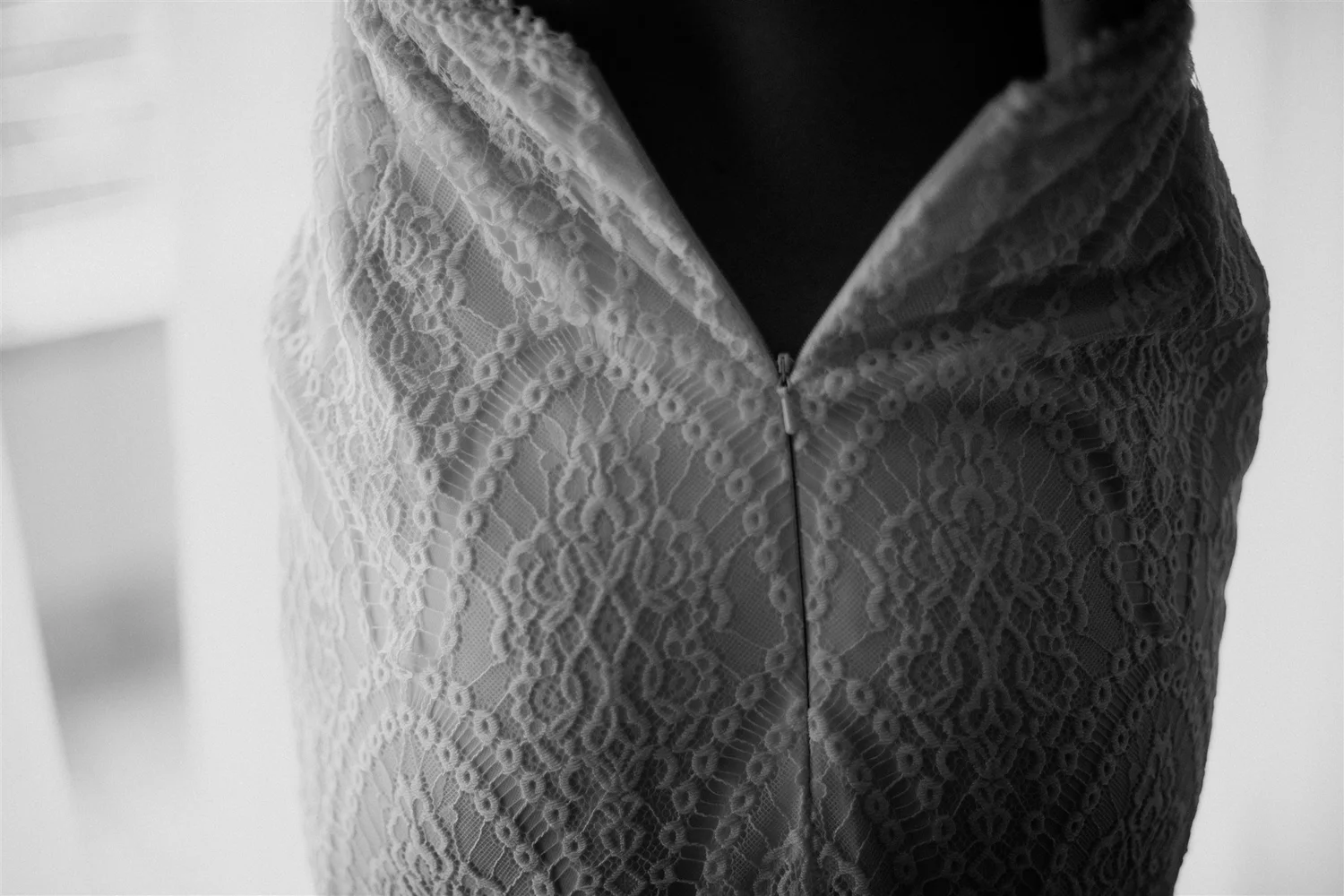 Close-up of a person wearing a dress with a lace overlay and a zipper in the front, in black and white.