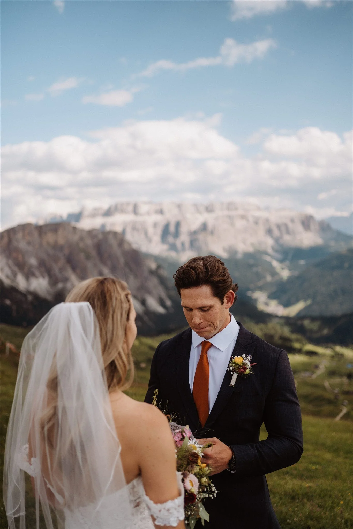 A bride and groom exchanging vows outdoors with mountain scenery in the background, during a wedding ceremony.