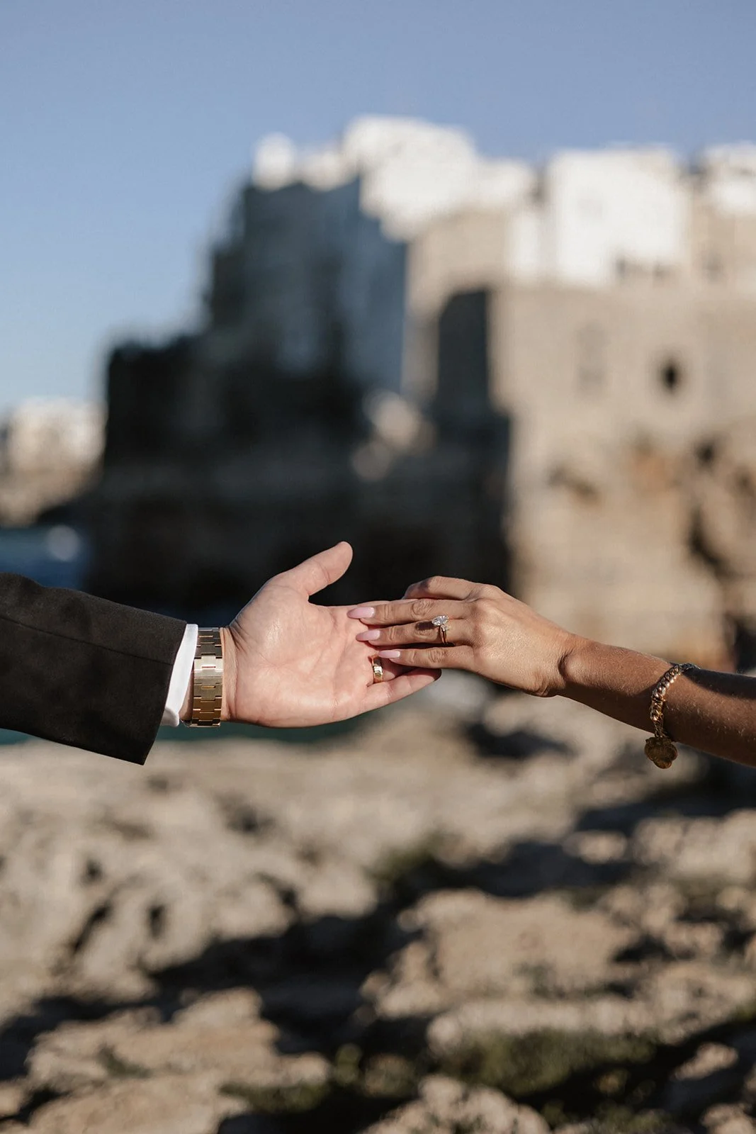 A man and a woman hold hands with a blurred historic building in the background, suggesting a romantic moment.