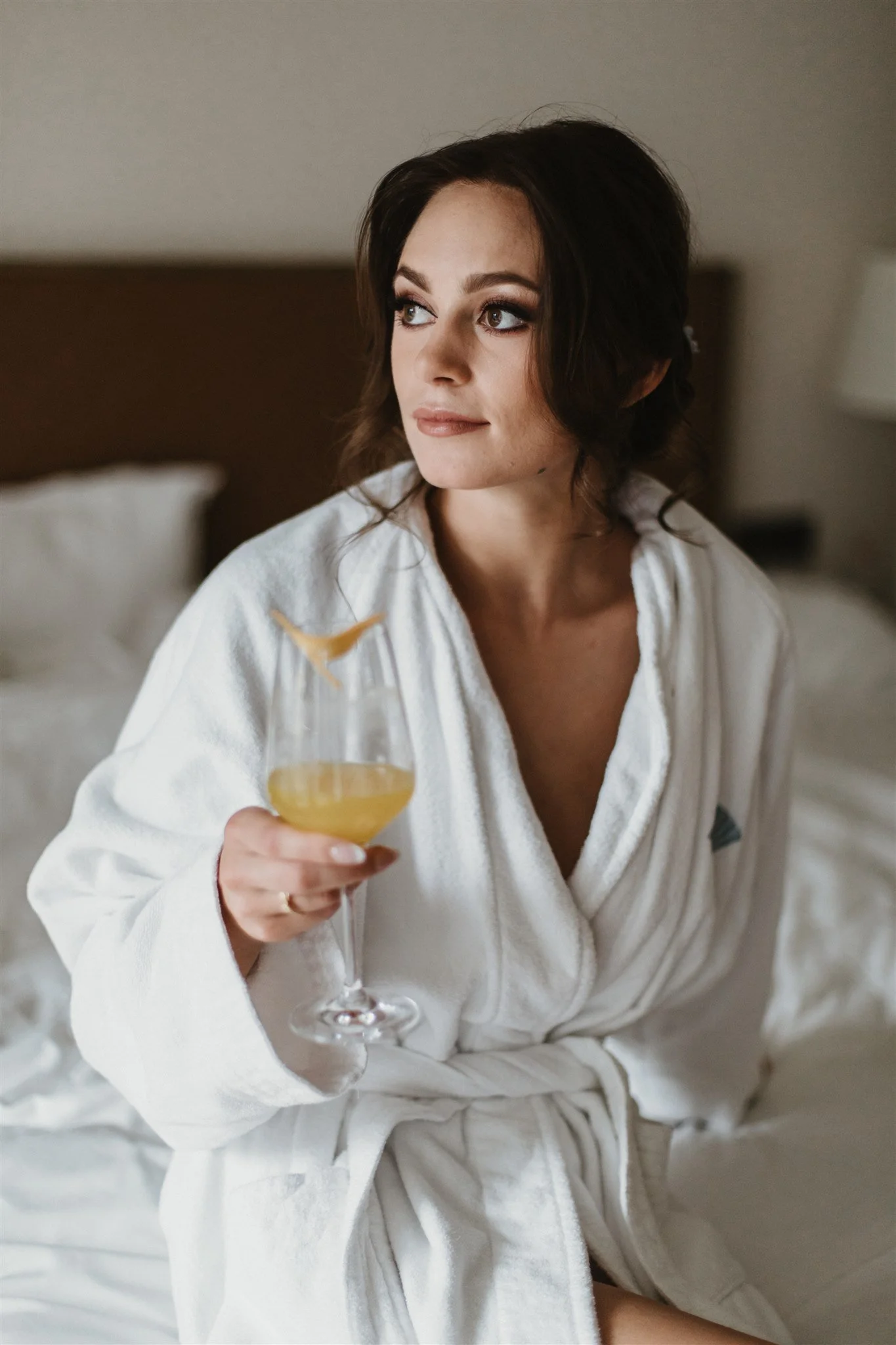 A woman in a white robe holding a glass of champagne in a bedroom.