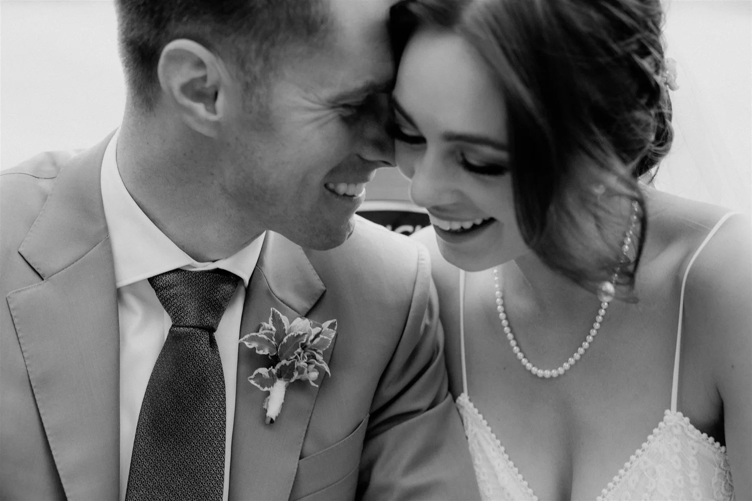 Black and white photo of a smiling man and woman with their foreheads and noses touching, dressed in formal attire and close together.