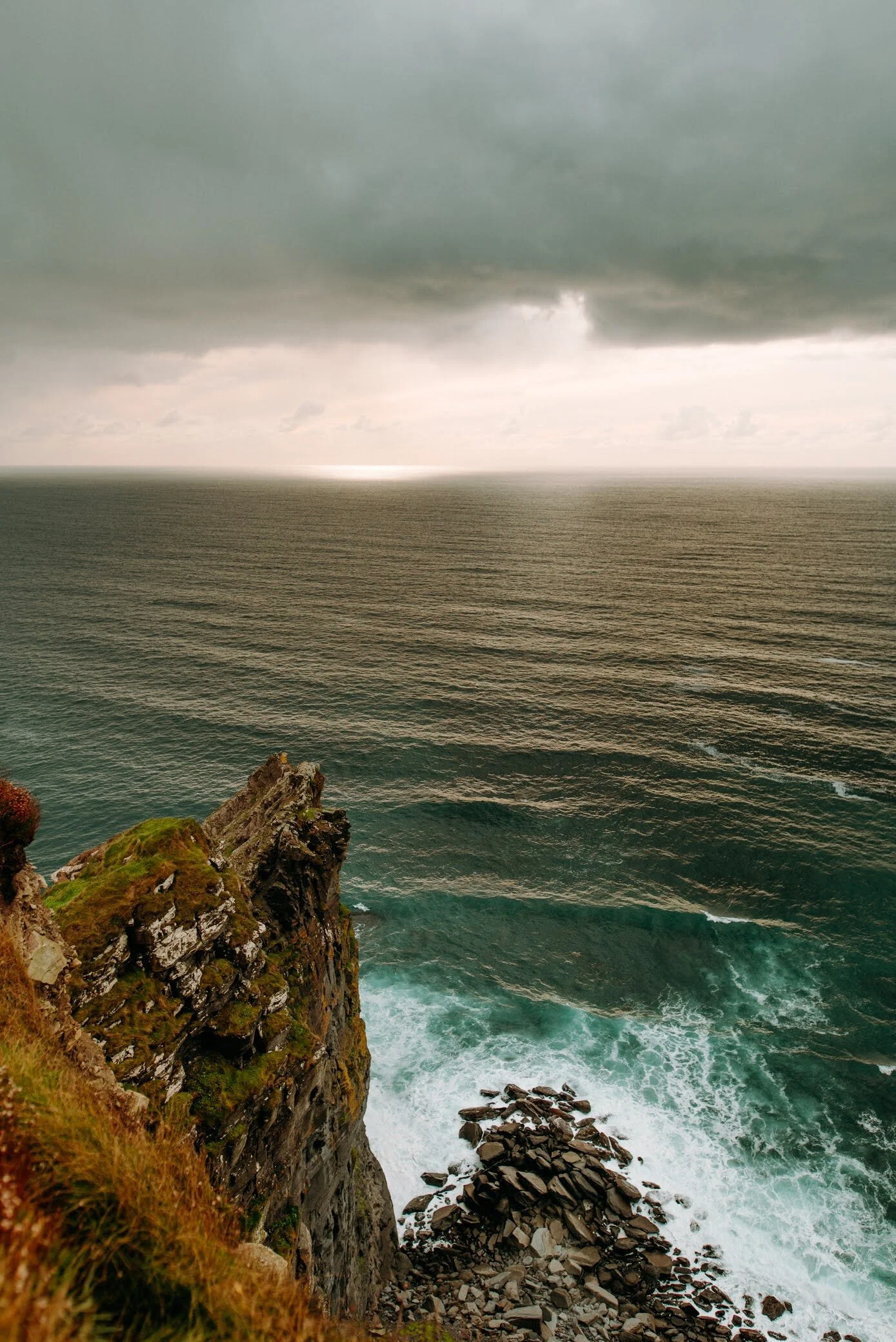 Stormy clouds over a rocky coastline, with the ocean's waves crashing against the rocks.