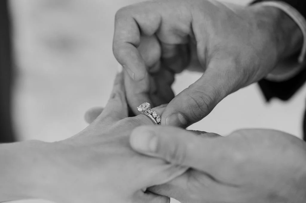A person's hand is being placed into a ring by another person's hand during a wedding or engagement ceremony.