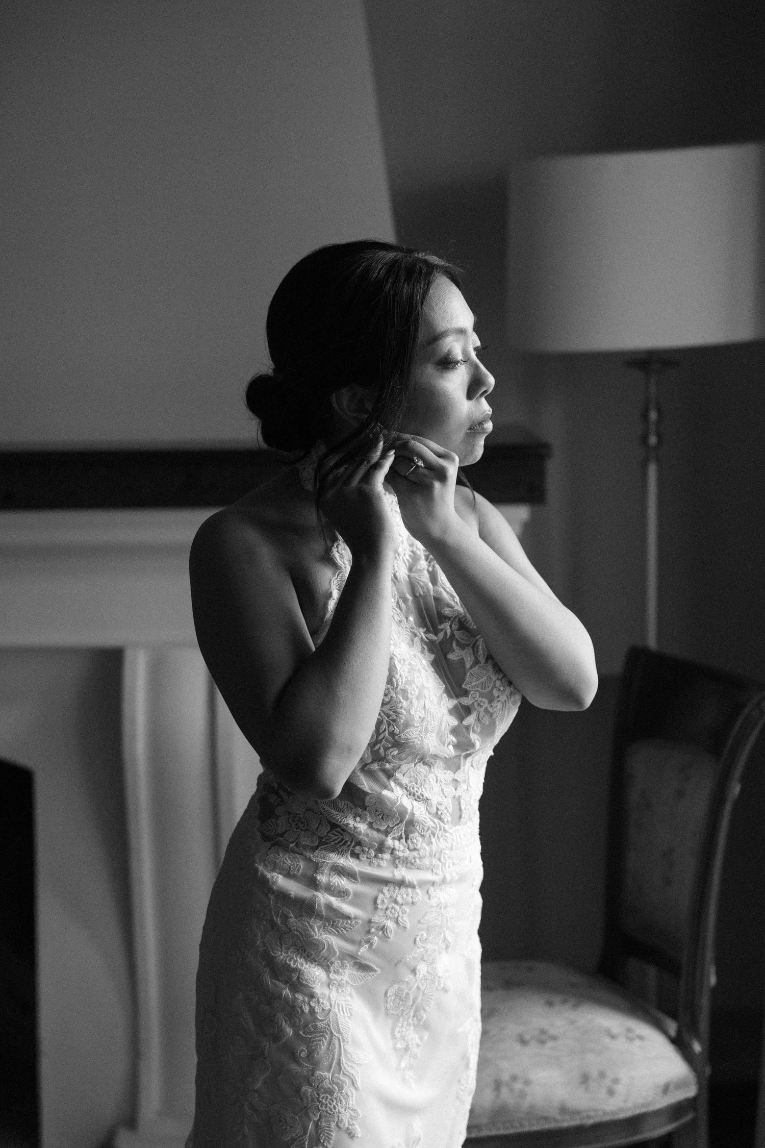 A woman in a wedding dress adjusting her earring in a dimly lit room.