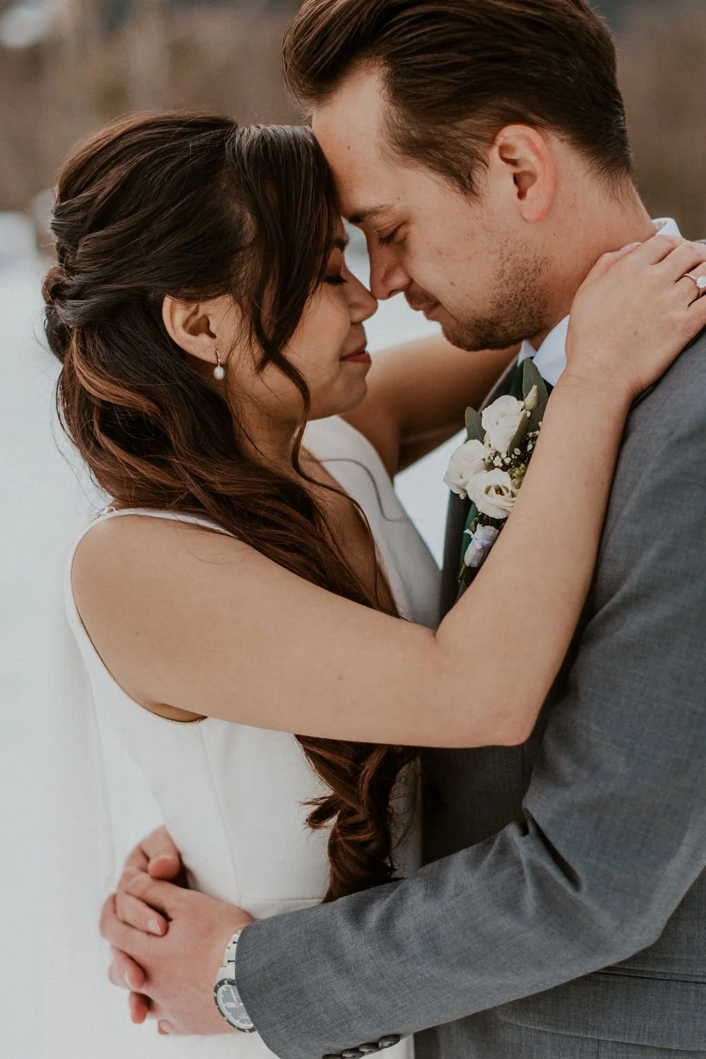 A bride and groom embrace with their foreheads touching, eyes closed, during their wedding ceremony outdoors.
