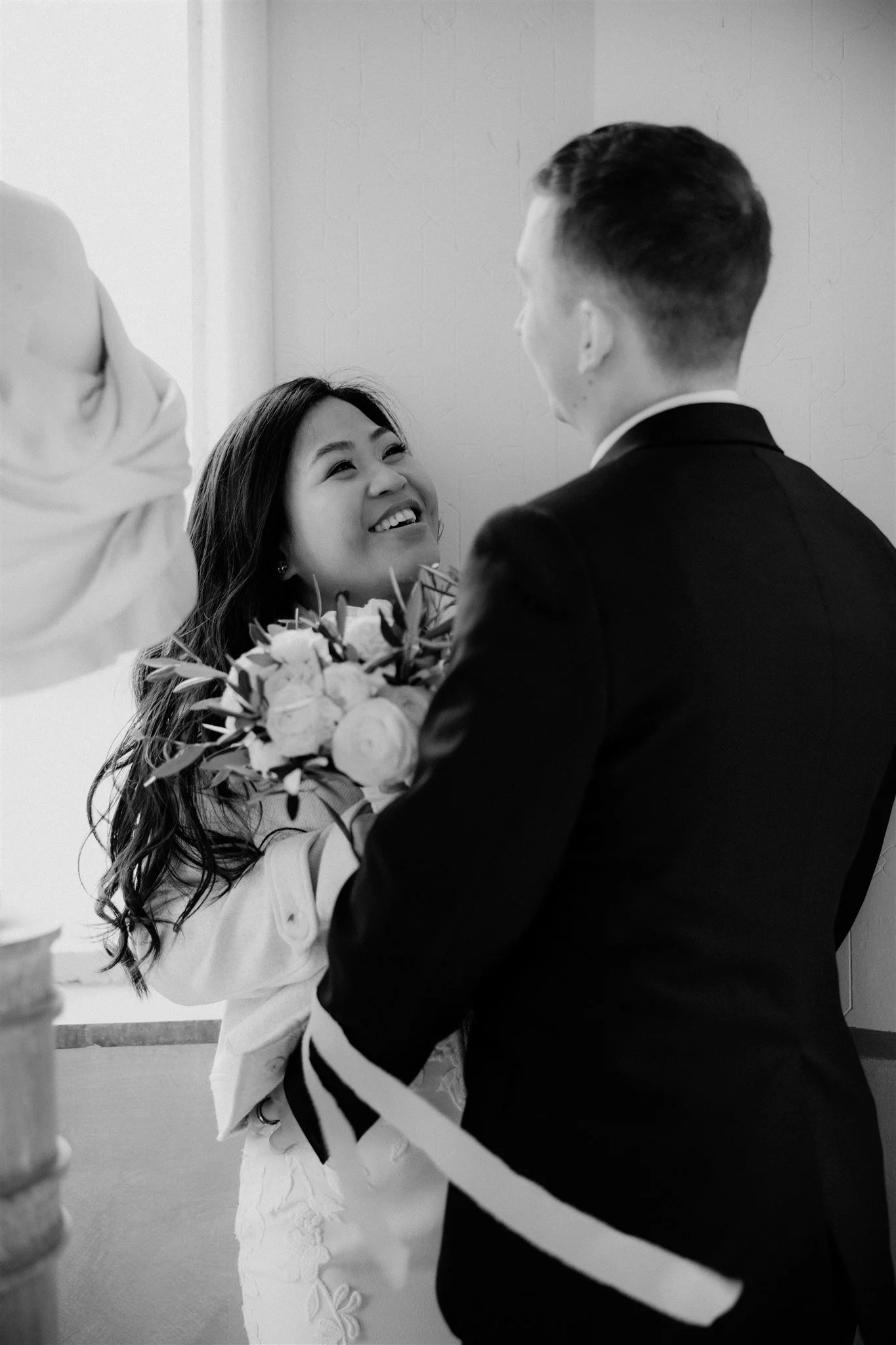 A woman smiling and looking up at a man, holding a bouquet of flowers, in a black and white photo, likely during a wedding or celebration.