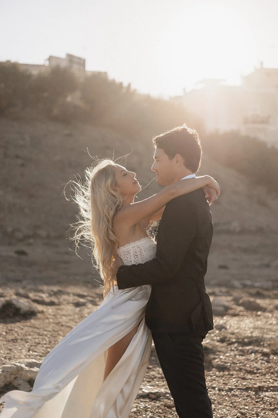A couple in wedding attire embracing on a beach during sunset.