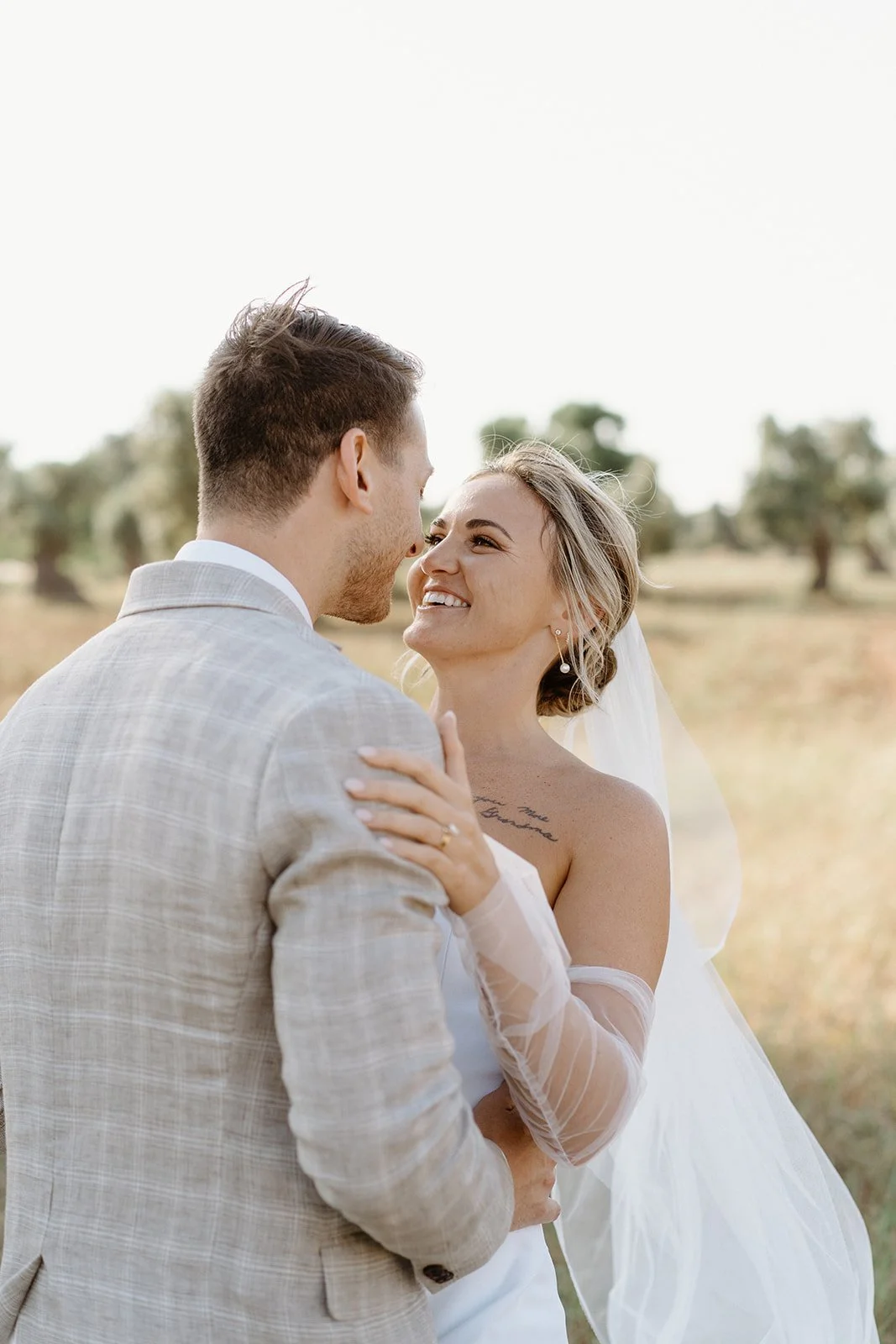 A bride and groom smiling and looking at each other outdoors on their wedding day.