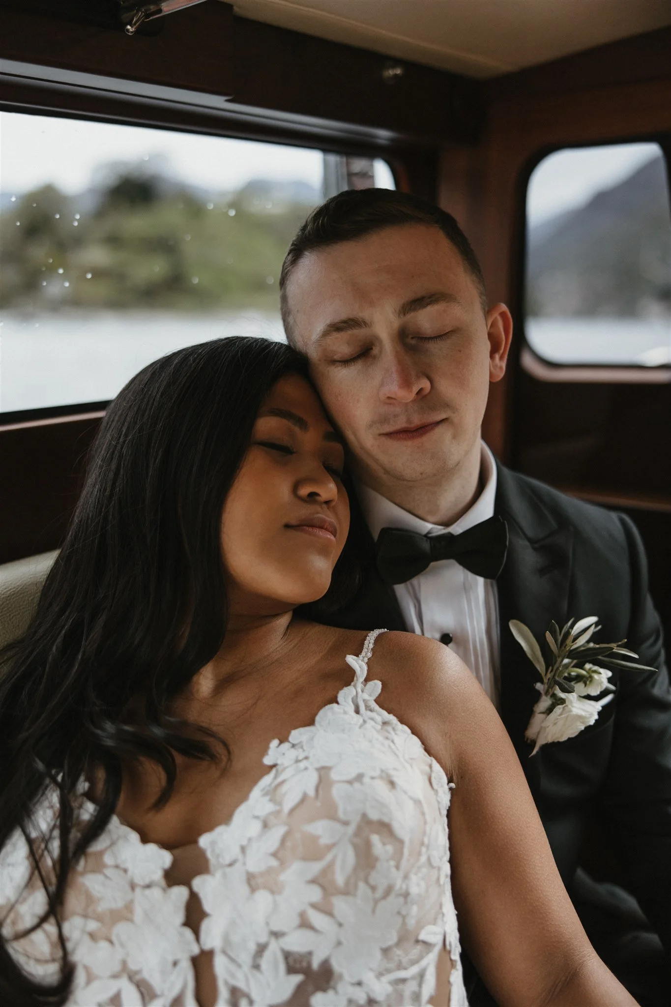 A bride and groom sitting close together with eyes closed, inside a vehicle.