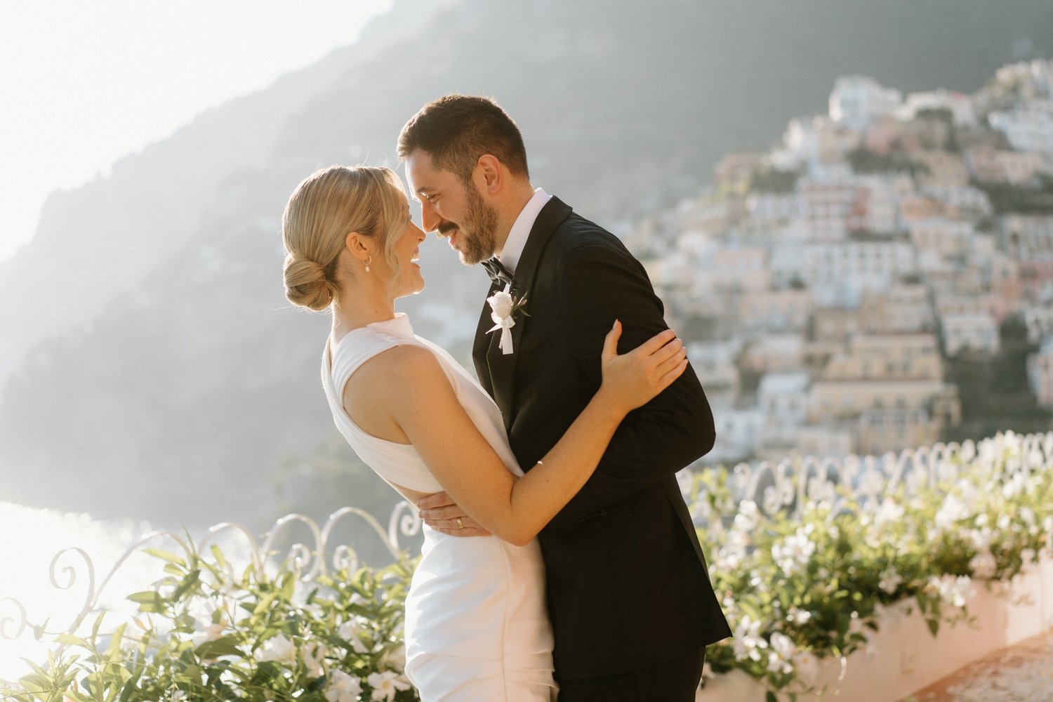 A bride and groom sharing a dance outdoors, with a cityscape and hillside in the background, decorated for a wedding.
