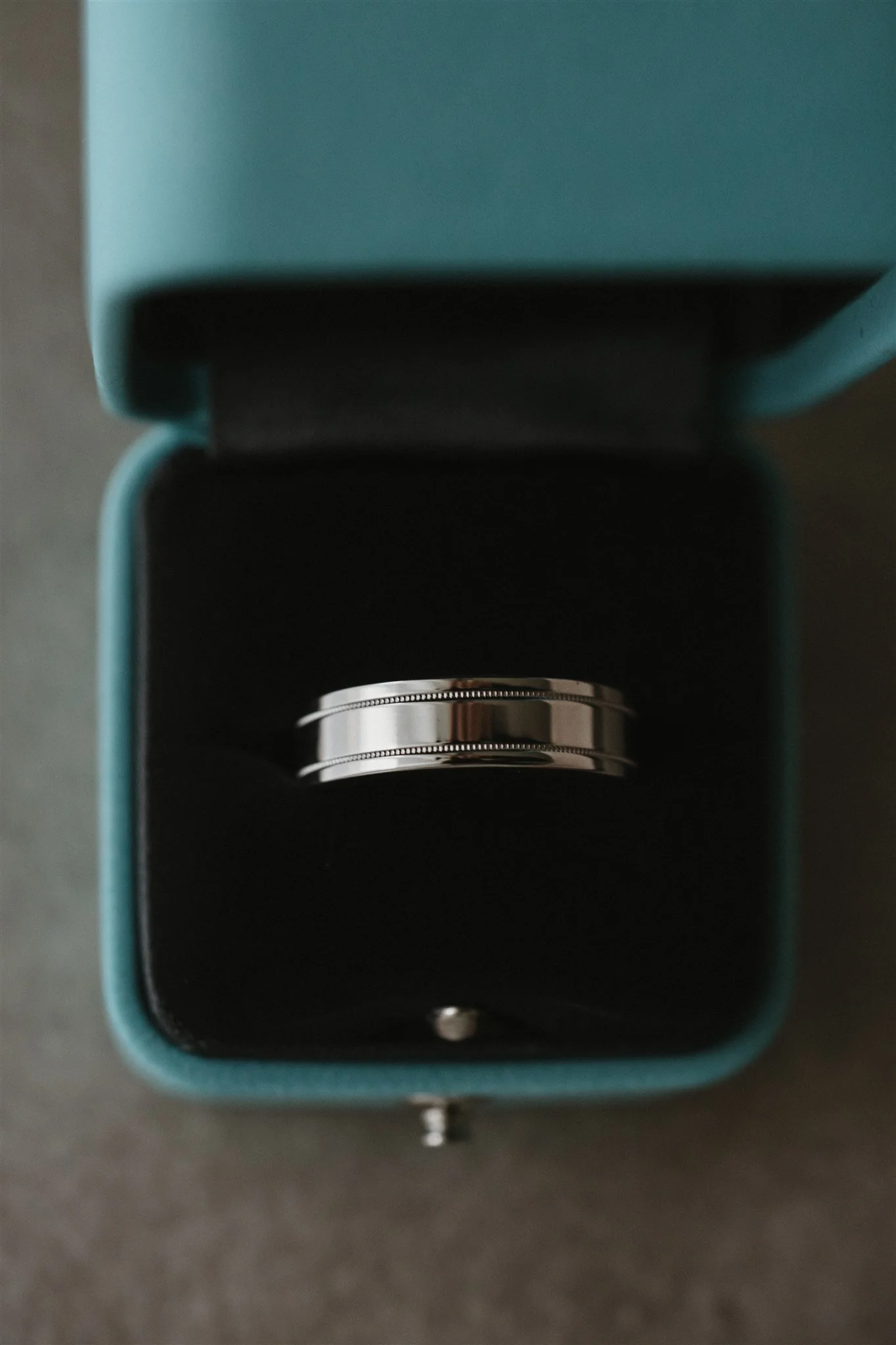 Close-up of a teal-colored box with a metallic ring inside, on a dark surface.