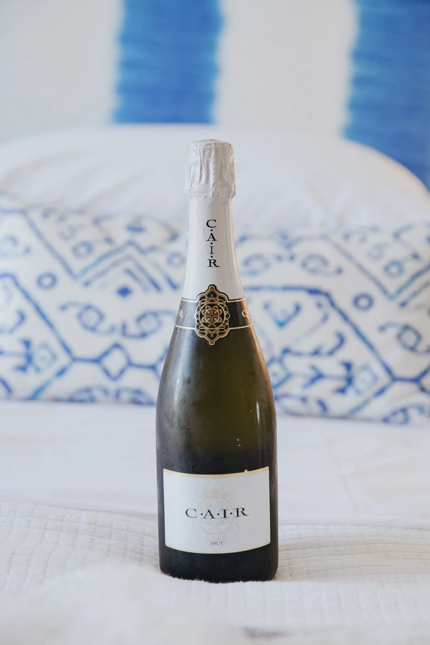 A bottle of C.A.T.R. Brut sparkling wine on a white surface with a blue and white patterned cloth in the background.