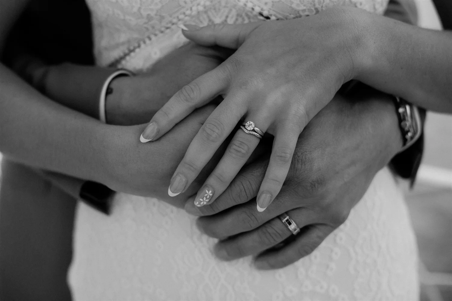 Close-up of a person's hand with a wedding ring, resting on another person's arm during a handshake or hug in black and white.