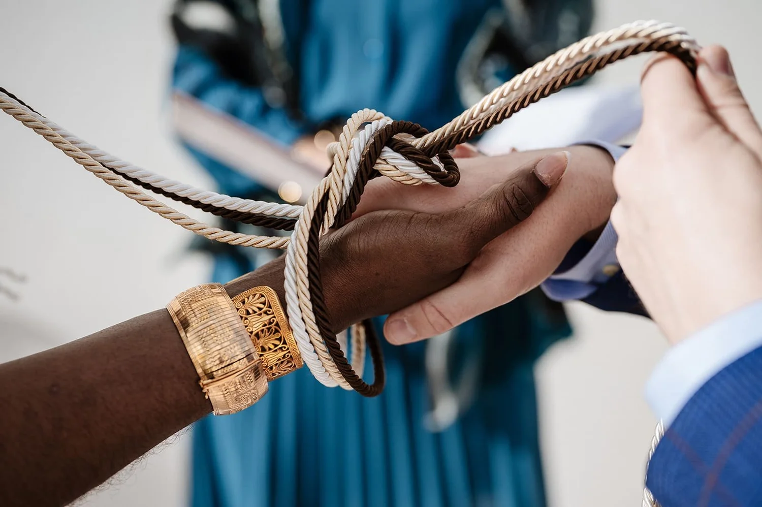 Close-up of two hands interlocked in a handshake, each person wearing different jewelry and clothing, with multicolored cords wrapped around their hands.