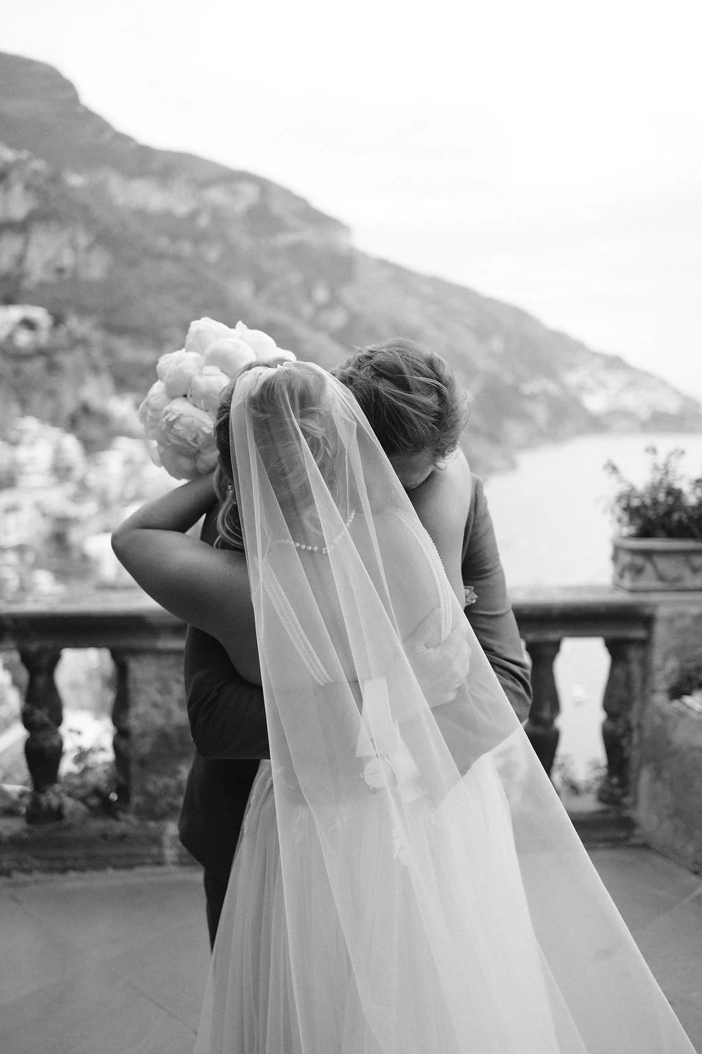 A bride and groom embrace during their wedding with a scenic hillside in the background.