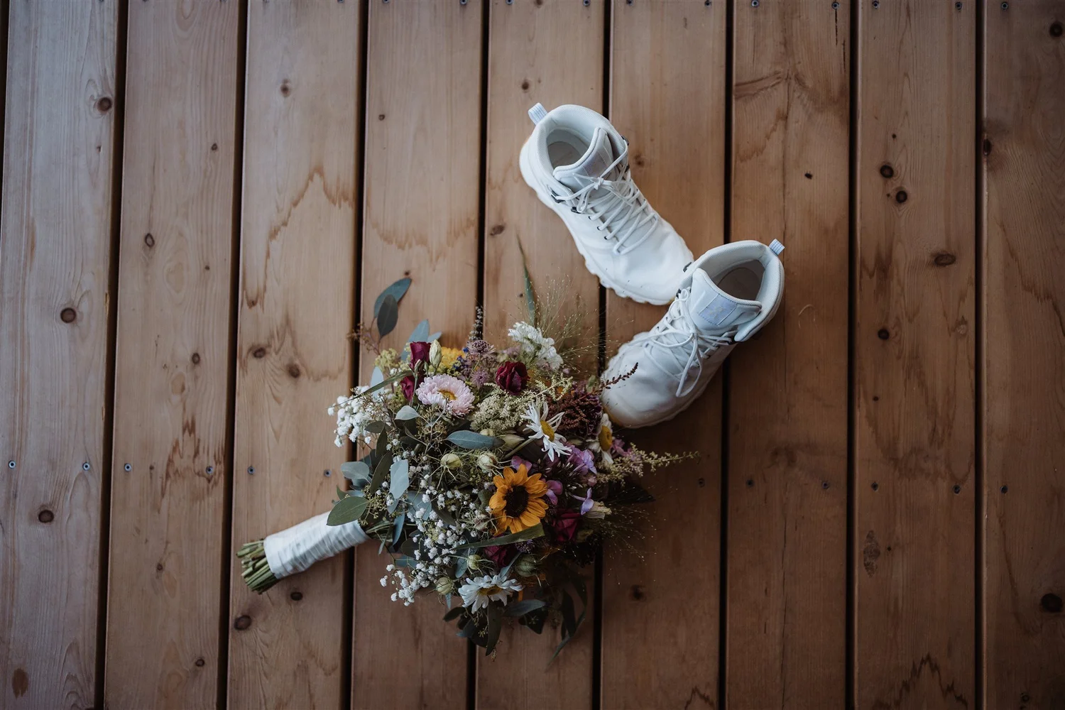 A bouquet of mixed flowers and greenery resting on a wooden floor.