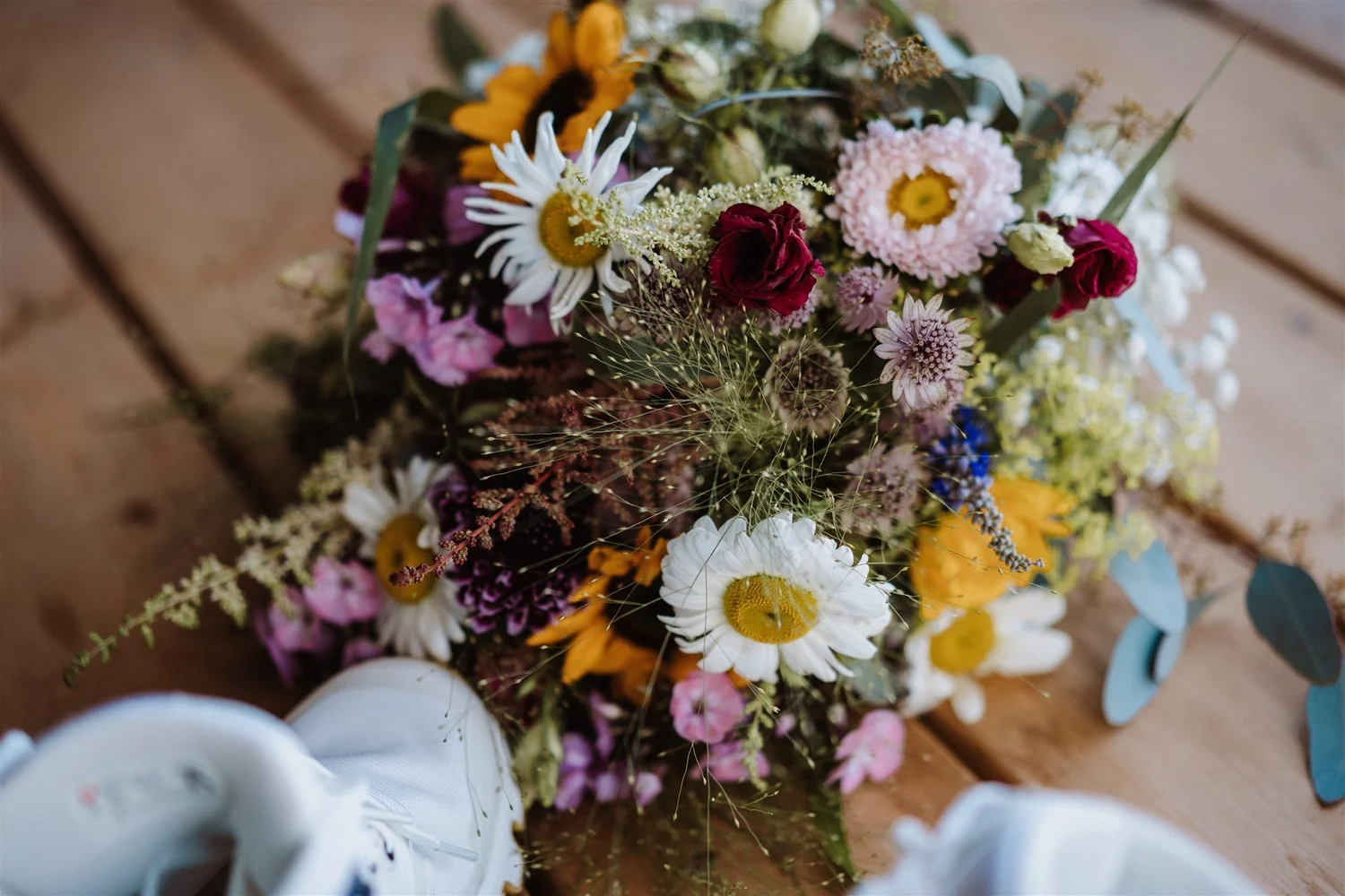 A colorful bouquet of mixed fresh flowers resting on a wooden surface, with white tableware partially visible in the foreground.