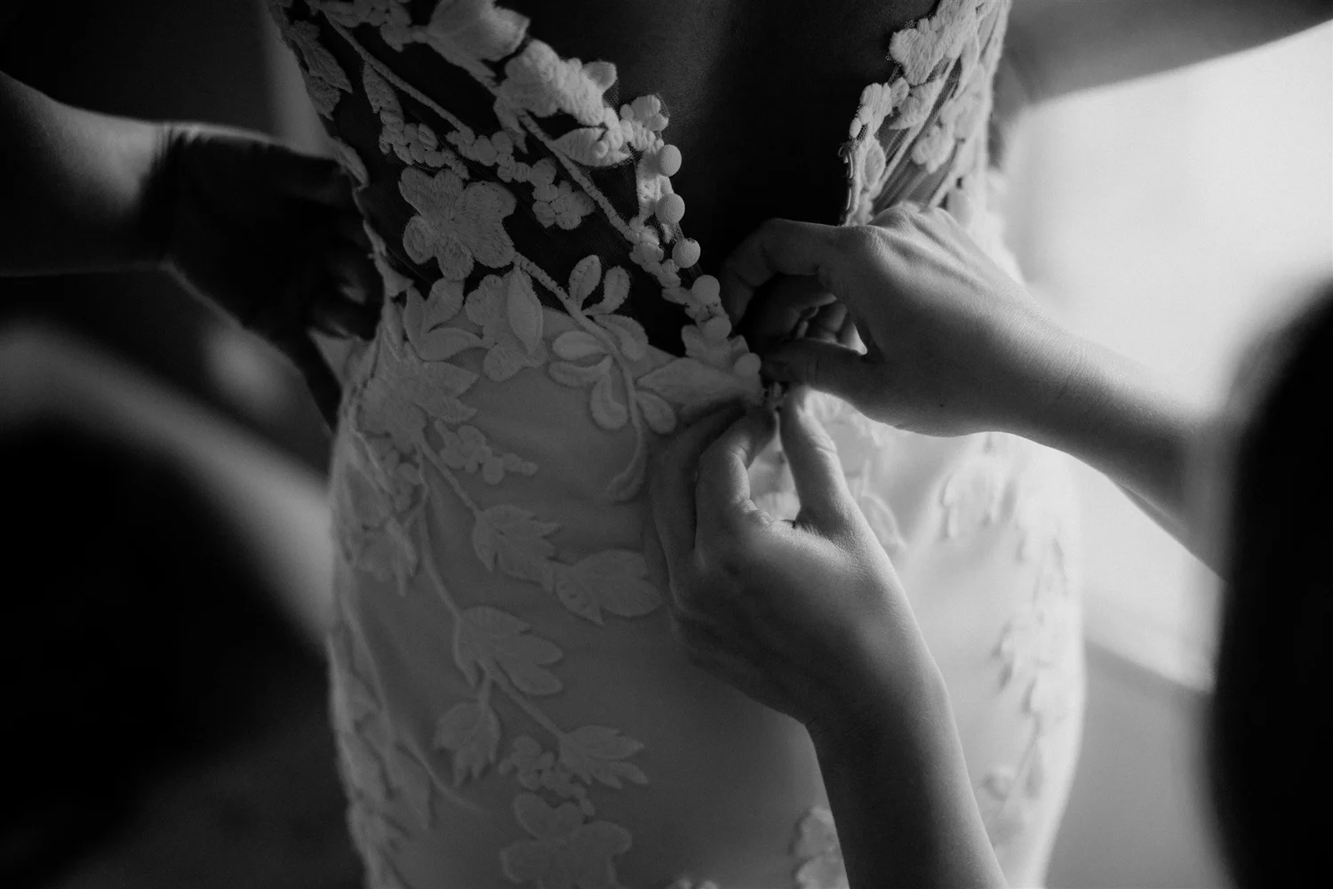 Close-up of hands adjusting a wedding dress with floral embroidery and 3D floral details, in black and white.