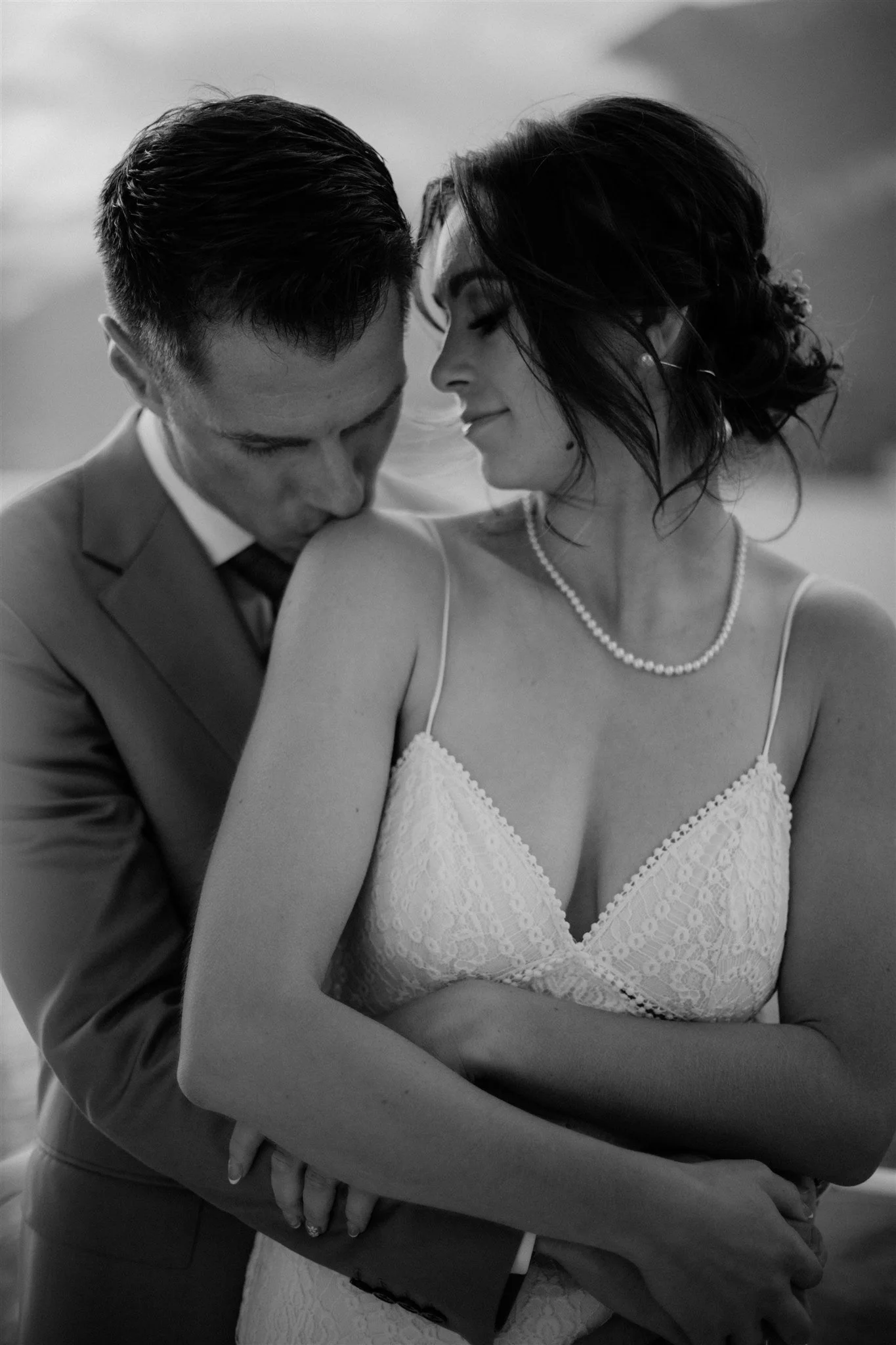 A black-and-white photograph of a man and woman in wedding attire sharing an intimate moment, with their foreheads touching and eyes closed.