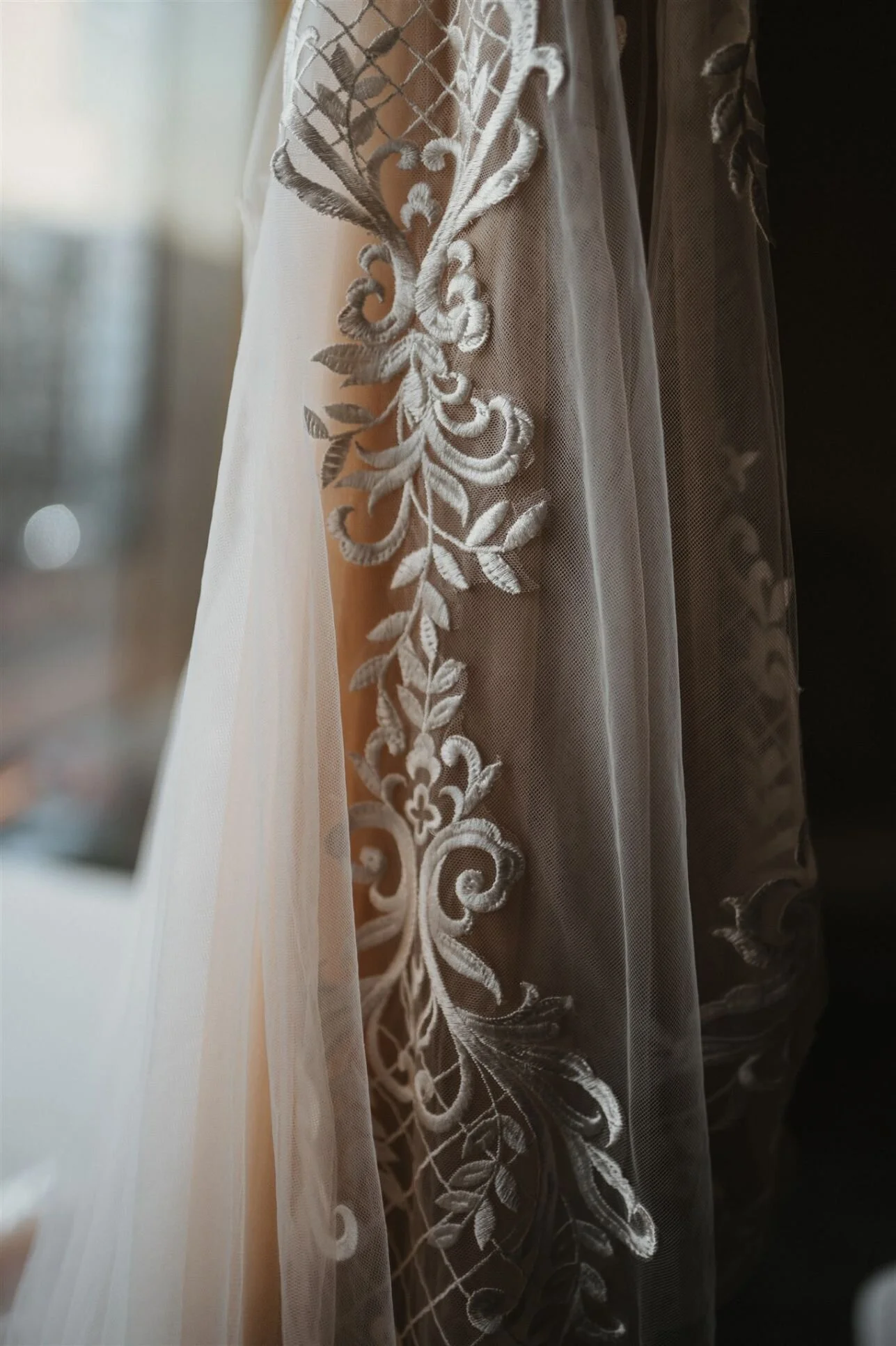 Close-up of sheer curtains with intricate white embroidery, hanging near a window with soft natural light.