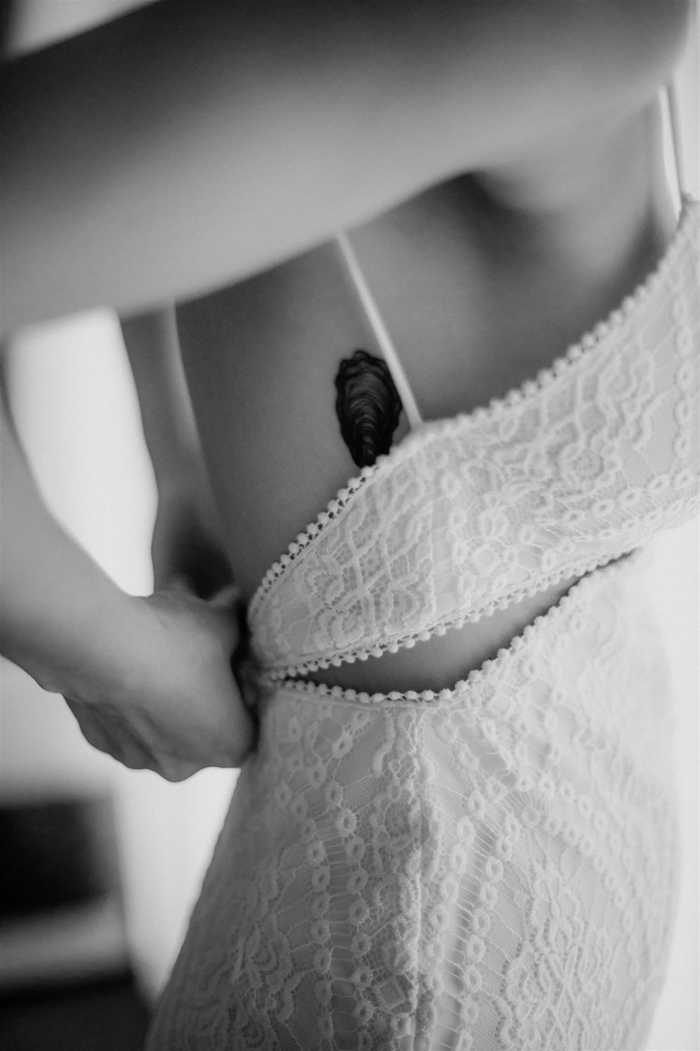 Close-up black and white photo of a woman wearing a lace dress, focusing on her torso and chest area.