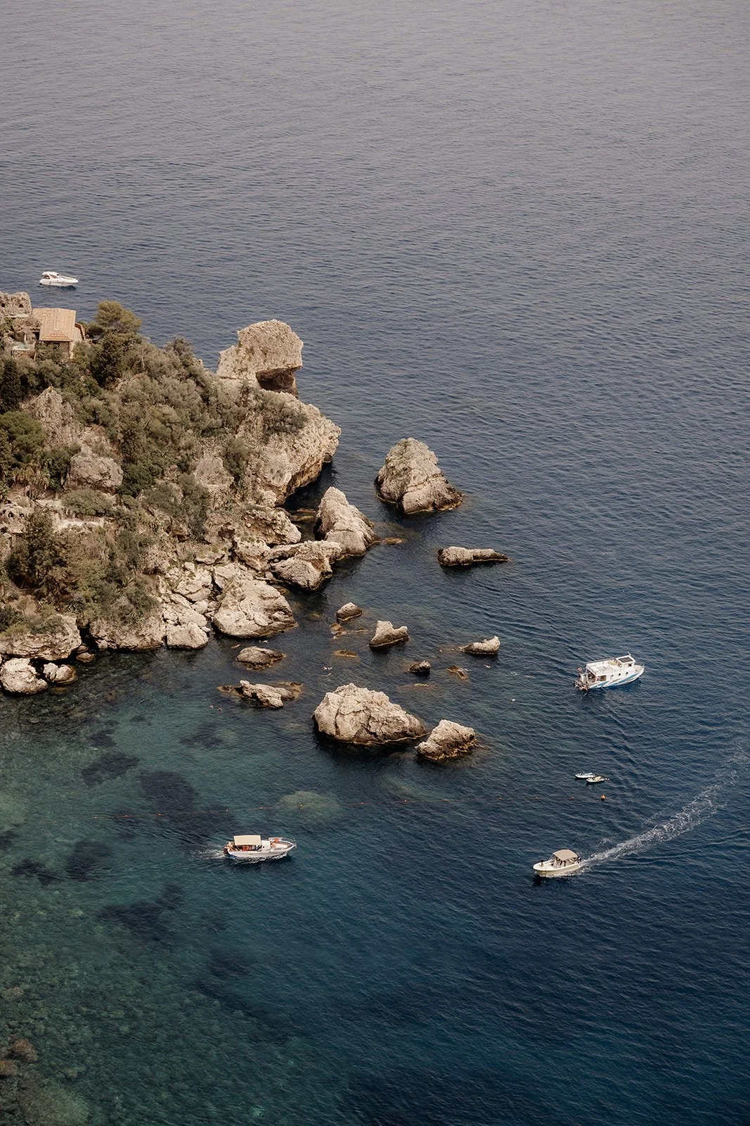Seaside landscape with rocky cliffs, boats, and calm water.