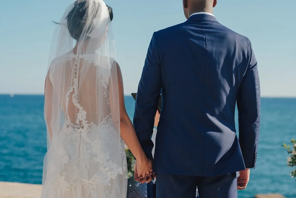Bride and groom holding hands during a beach wedding ceremony, with the ocean in the background.