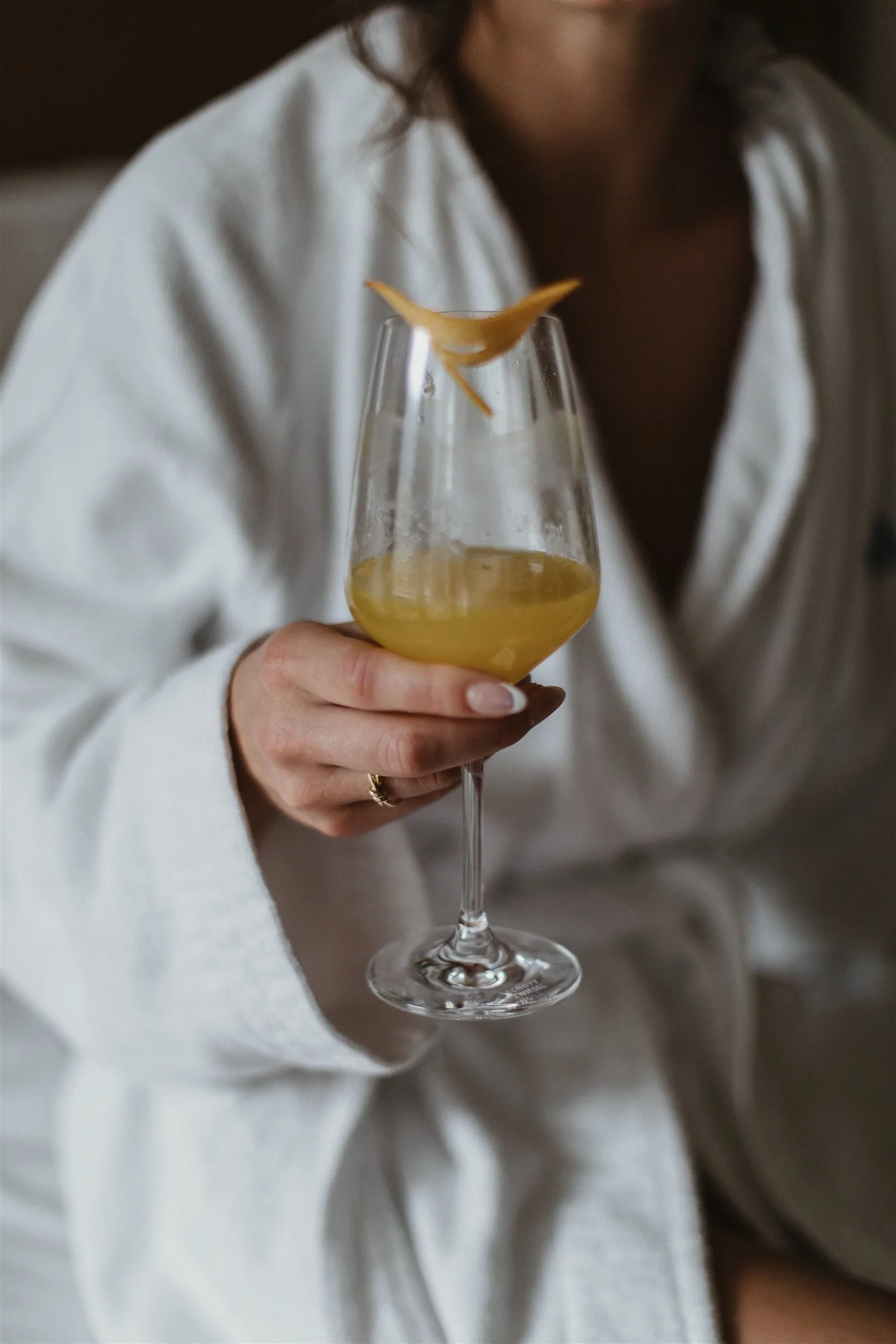 Person holding a glass of yellow wine with a chicken-shaped garnish on the rim, person wearing a white shirt.